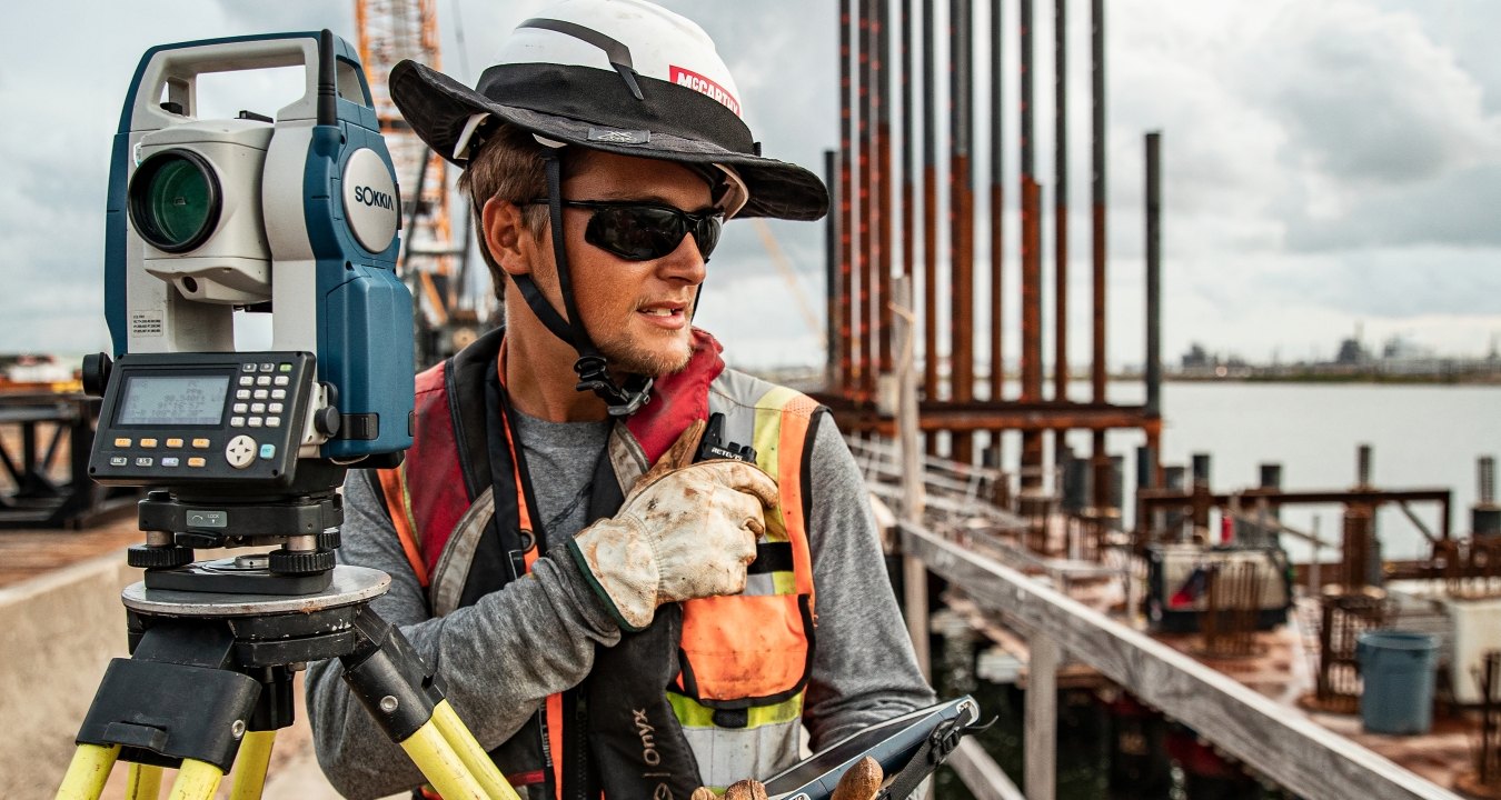 A construction worker operates survey equipment on a busy jobsite.