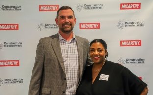 Two people standing in front of a Construction Inclusion Week banner. 