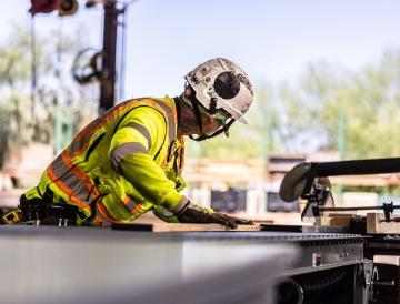 A person working with full PPE and cutting a piece of wood