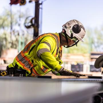 A person working with full PPE and cutting a piece of wood