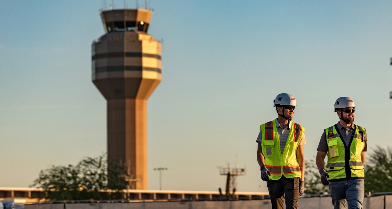 Two people walking with an airport control tower in the background