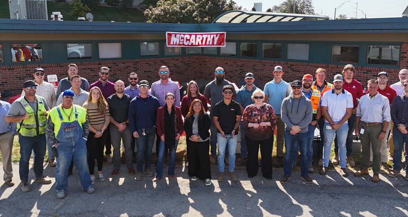 A group of people standing in front of a building with the McCarthy logo hanging in the background.