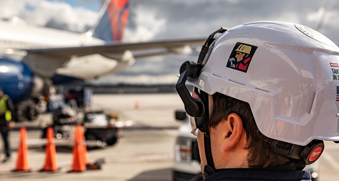 A person wearing PPE in the foreground with an airplane in the background
