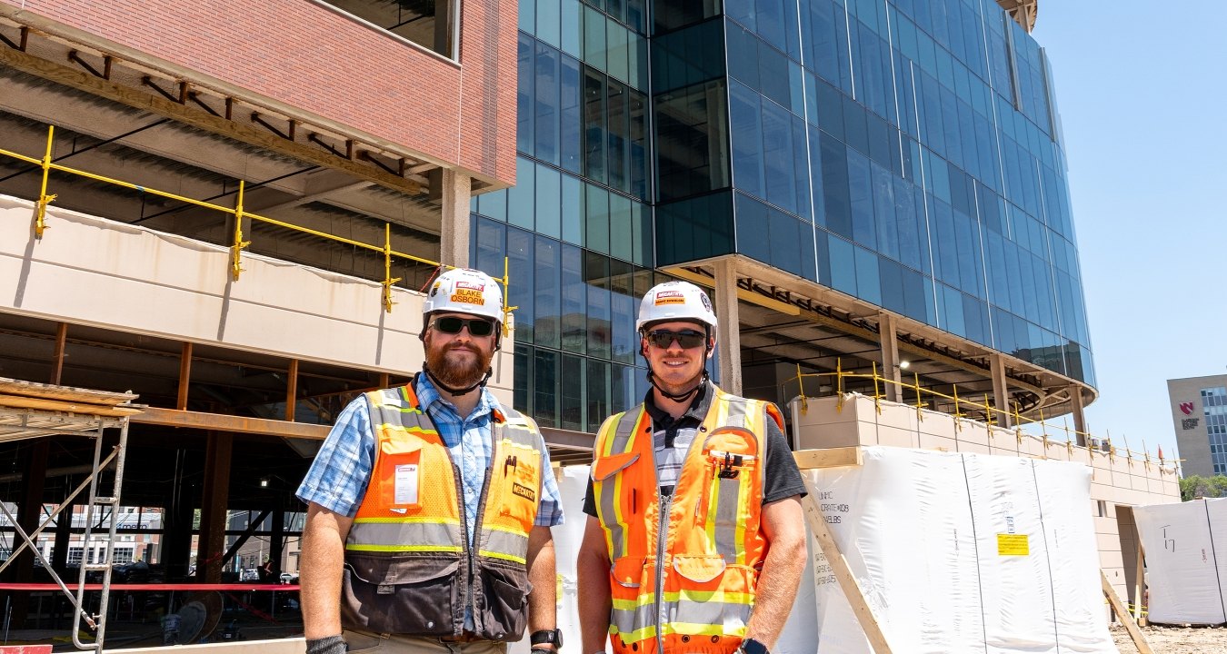 Two people standing in front of a building under construction wearing PPE