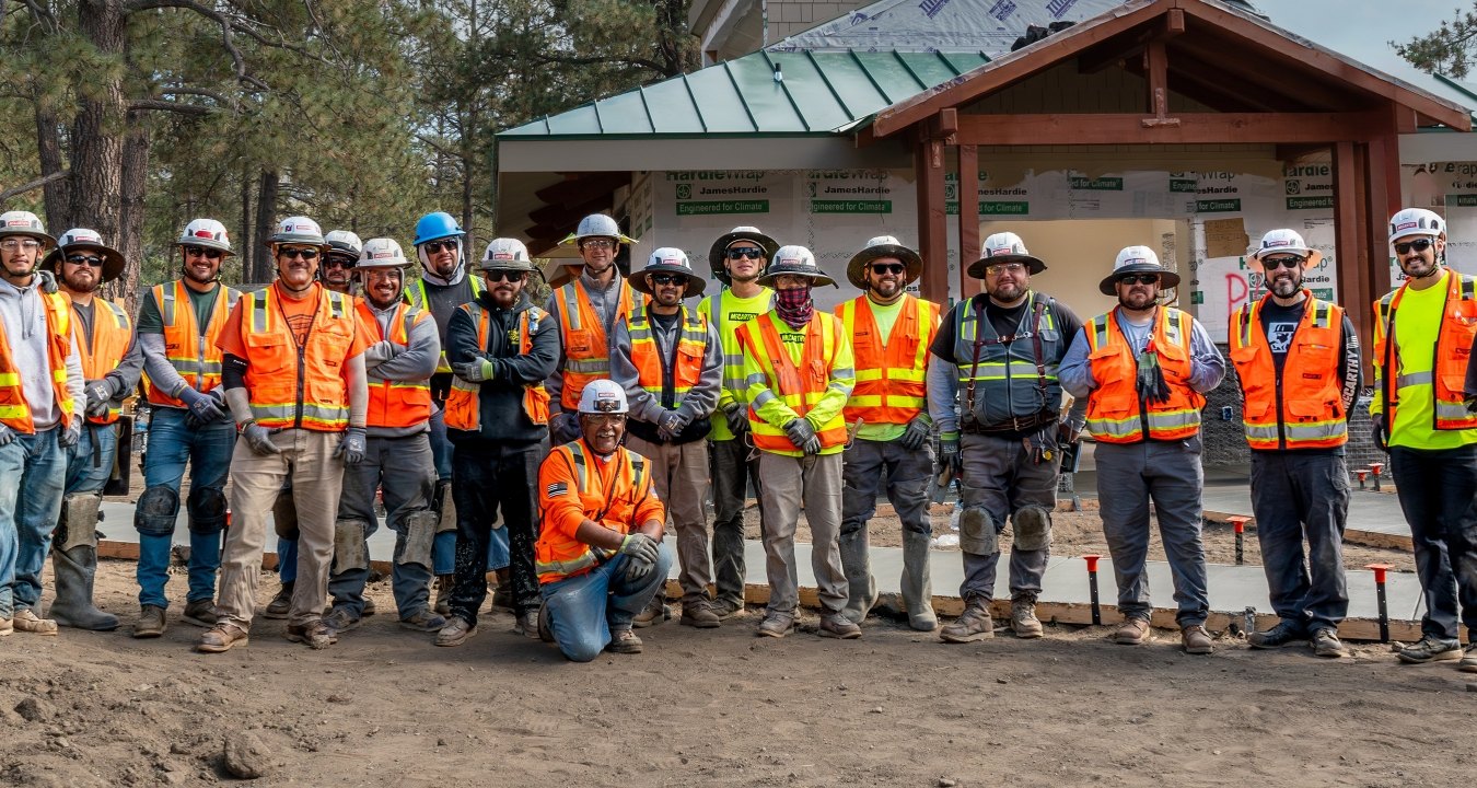 A group of people wearing PPE posing in front of a building under construction.