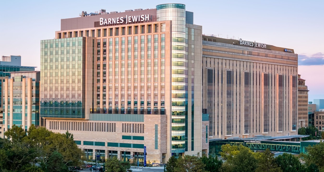 Evening view of the Barnes-Jewish Hospital towers with glass façade reflecting the sunset above treetops