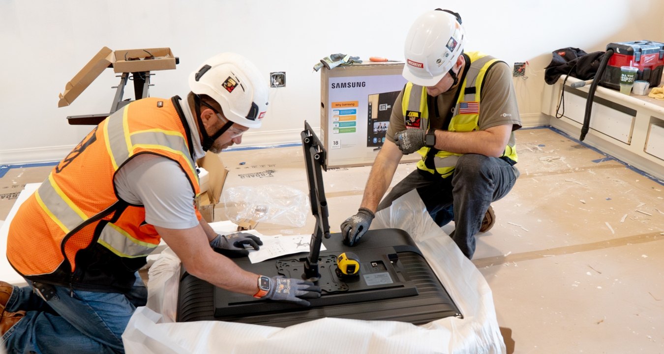 Two people wearing PPE and working on a TV