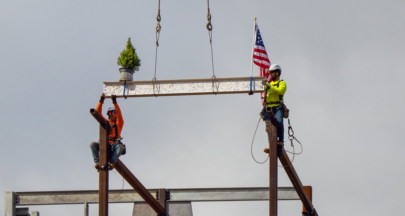 Two people wearing PPE placing the final beam on top of the structure