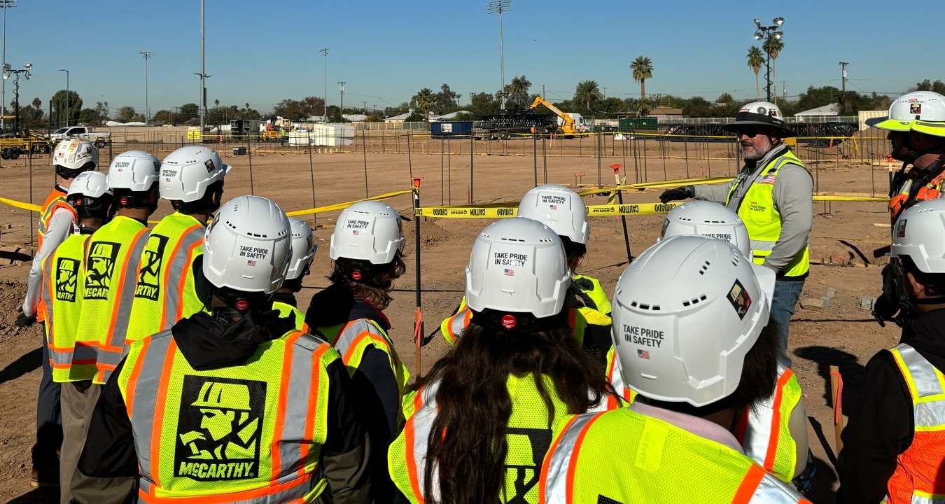 A group of people wearing PPE listening to a person speak