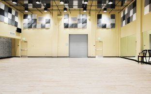 Empty studio room with tall ceilings and a mirror on the righthand side wall.