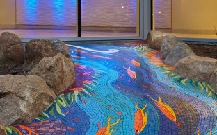 Outdoor children's play area with ocean-themed tiled walkway bordered with stones