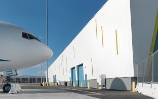 The nose of an airplane facing a building.