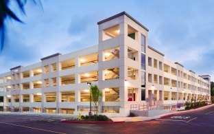 Scripps Health Parking Structure Exterior with Blue Sky, Roadway and Lights on in Structure