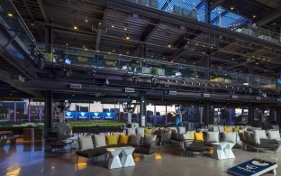 Photo showing two levels of the topgolf interior with couches, tables, and bays