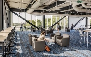 A large open area with lounge chairs, tables, and chairs. Large glass windows