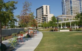 A pathway through the green park with tall buildings in the background