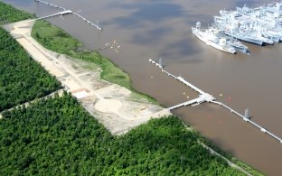 Aerial view of the facility over the water with boats in the background and greenery on land in the foreground