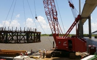 A crane on a barge in the water during construction with people working