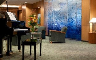 Lobby area with chairs and a blue artsy wall, with a grand piano on the left side of the photo