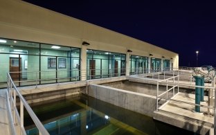 Water and pipes in front of the water treatment plant building at nighttime