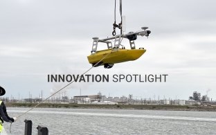 A person hoisting an unmanned survey vessel into the water
