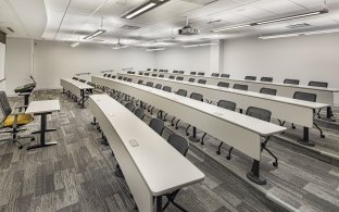 A lecture-style classroom with elevated, staircase seating and tables