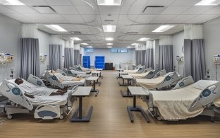 A room with rows of hospital beds and practice dummies for healthcare education. 