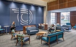 View of a waiting room with couches and chairs and a few people sitting. 