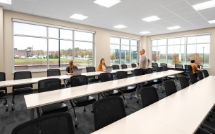 A classroom style room with long tables and rows of chairs at each long table.