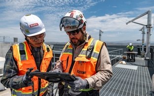 Two people wearing construction PPE at a jobsite while looking at a tablet. 