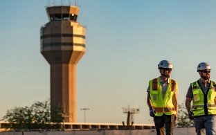 Two people walking with an airport control tower in the background