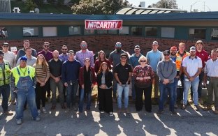 A group of people standing in front of a building with the McCarthy logo hanging in the background.