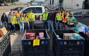 A group of people standing near a few cases of donated food items