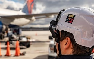 A person wearing PPE in the foreground with an airplane in the background