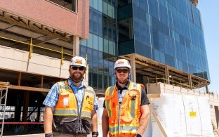 Two people standing in front of a building under construction wearing PPE