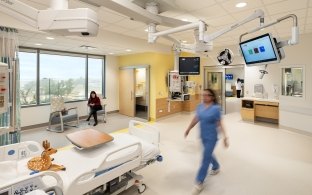 A person walking toward a bed in a patient room in the PICU