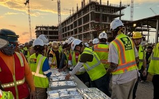 A group of people grabbing wrapped breakfast burritos 