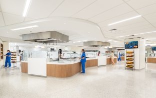 Bright hospital cafeteria with staff and visitors ordering food at multiple serving stations