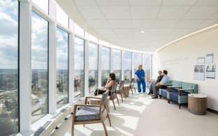 Sunlit hospital waiting area with floor-to-ceiling windows and patients talking with a nurse.