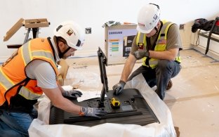 Two people wearing PPE and working on a TV