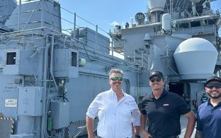 Three people standing in front of a military ship