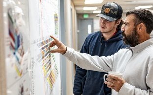Two people looking at paperwork on the wall. 