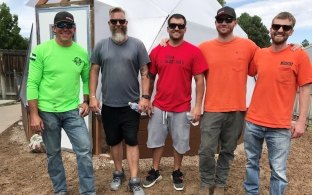 	Five McCarthy team members in work gear pose outside a small building during a Heart Hats volunteer build.