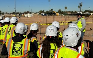 A group of people wearing PPE listening to a person speak