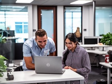 Two people sitting at a desk looking at a computer.