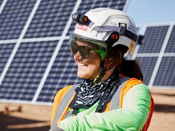 A person wearing PPE smiling with solar panels in the background
