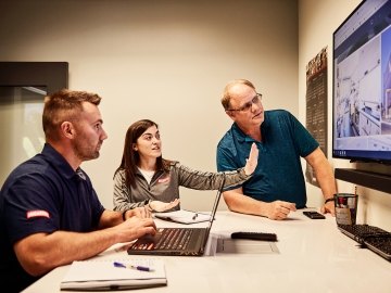 Three McCarthy employees viewing a large monitor displaying project renderings