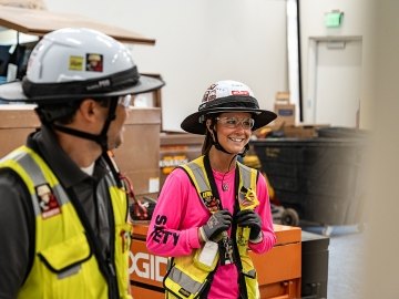 Two people wearing PPE and talking while one person is smiling