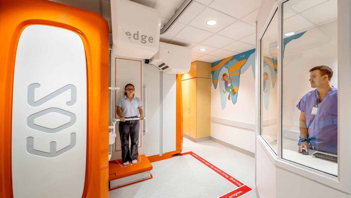 A person standing in the EOS machine while someone else looks on
