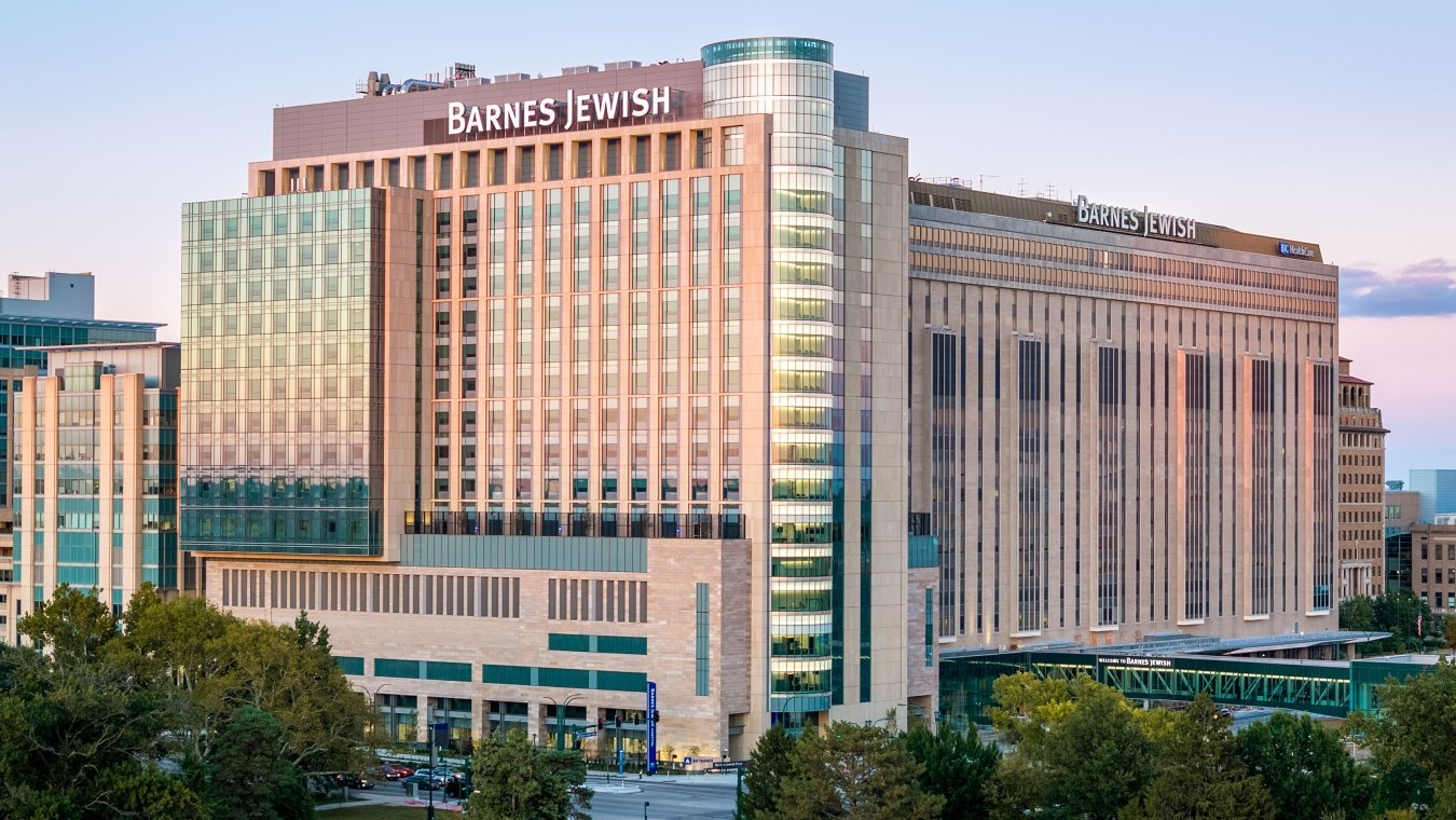 Evening view of the Barnes-Jewish Hospital towers with glass façade reflecting the sunset above treetops